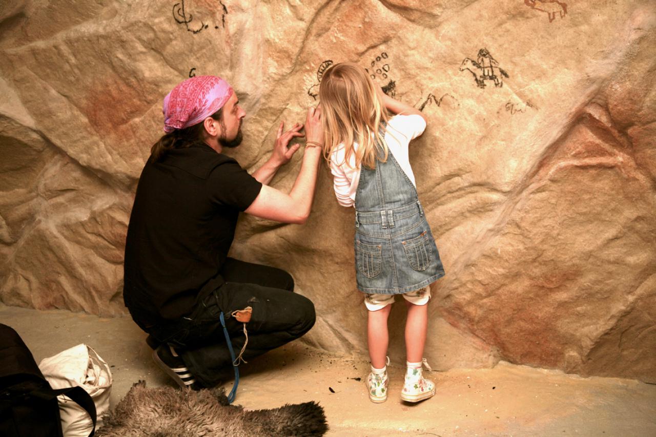 Archäologisches Museum Hamburg. Ein Mann und ein Kind malen an einer, einer Höhle nachempfundenen Wand.