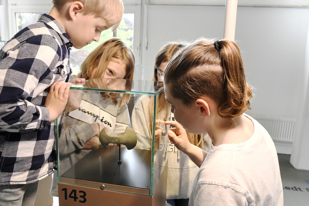 Kinder sehen sich in einer Vitrine eine Axt aus der Steinzeit an.