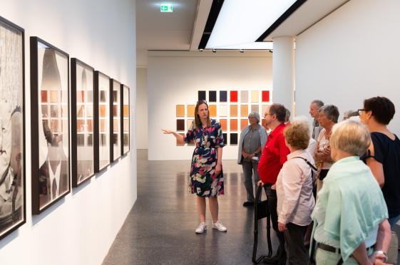 Gruppenführung - © Bucerius Kunst Forum, Foto: Ulrich Perrey Das Foto zeigt eine Gruppe von Museumsbesuchern, welche mit Abstand ein Gemälde in einer Galerie betrachten. Zudem sieht man einen Museums Guide, welcher der Gruppe weitere Informationen zugeben scheint.