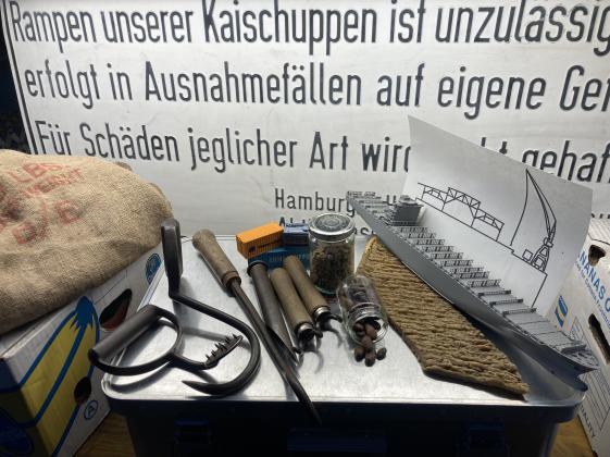 Materialkoffer Museum zum Anfassen für blinde und seheingeschränkte Menschen PEKING - © Museumsdienst Hamburg, Jens Fömpe Das Foto zeigt einen Materialkoffer voller Objekte, die bei der Führung zum Einsatz kommen: Seesack, Griepen, Bananenkisten, Containermodelle, Geruchsproben von Kakao und Kaffeebohnen, ein graues Modellschiff und Schwellkopien.