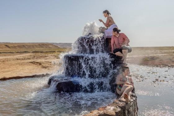 Battered Waters - © Anush Babajanyan Zu sehen ist ein Brunnen in einer trockenen Umgebung. An dem Brunnen sitzen drei Personen.